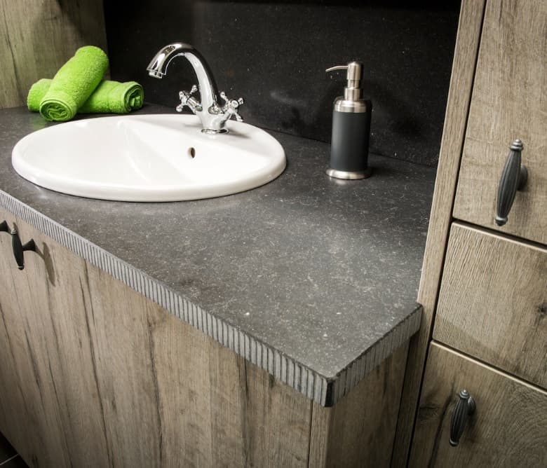Detail van een badmeubel in vergrijsd hout met een inbouwwastafel in donkere natuursteen