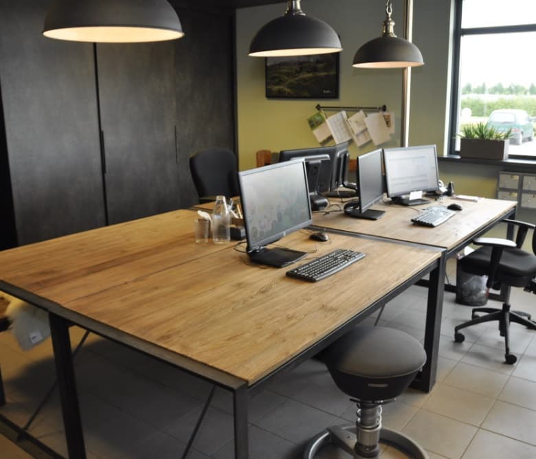 Kantoor in industriële stijl met houten werkbladen op zwart stalen onderstellen en hanglampen
