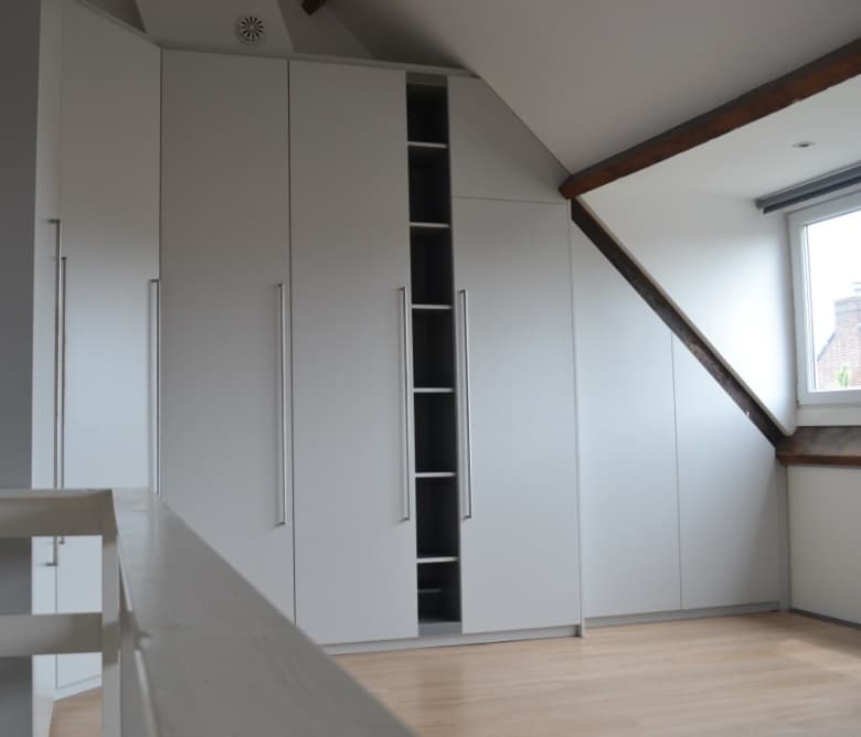 Wandkast op maat langs een trap, met een schuine zijkant en open nissen in wit