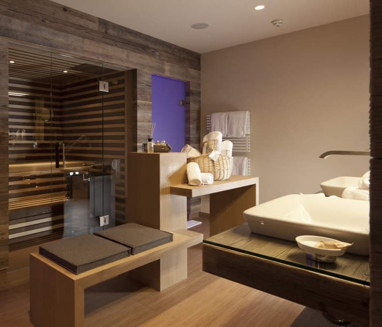 Wellnessruimte met een sauna achter glas, een eiken maatwerkbank en een ingebouwd bad