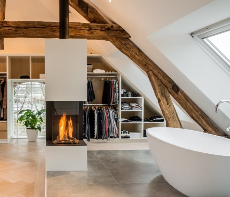Open badkamer onder het dak met een vrijstaand bad, een haard en een open kledingkast op maat