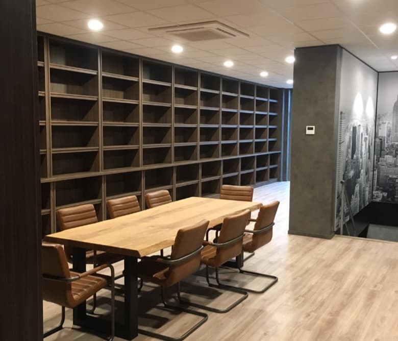 Vergaderruimte met een lange tafel en een wand van maatwerk vakkenkast in donker hout