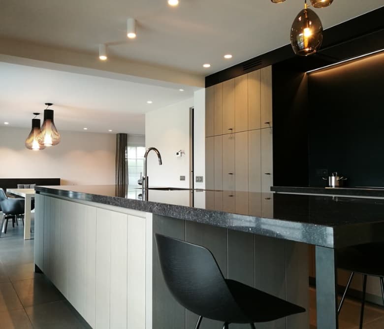 Keuken met witte fronten tegen een zwarte wand, composiet werkblad en een strak vormgegeven kookeiland