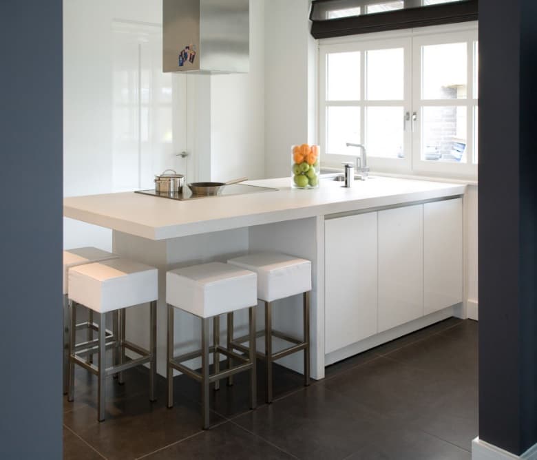 Matwitte keuken met greeplijst en Dekton werkblad, met een kookeiland en witte barkrukken bij het raam