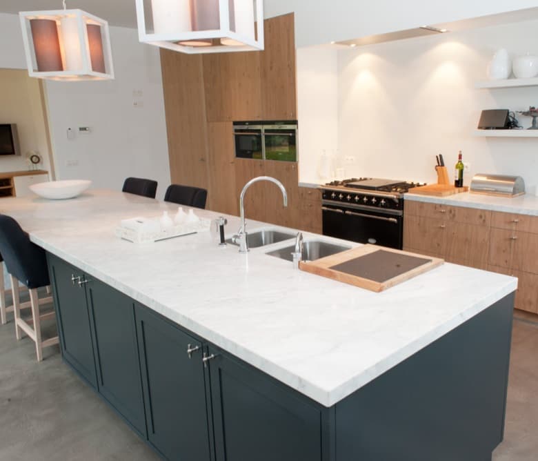 Keuken met donkerblauw kookeiland, licht Dekton werkblad en hoge kasten in eiken naast een zwart fornuis